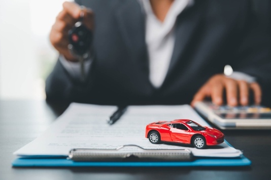 Person holding car keys in front of a clipboard with a toy car