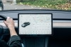 A view of a driver's right hand on the steering wheel next to a large car monitor screen.