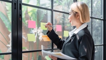 Woman in UX design is card sorting using sticky notes on a window