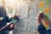 A closeup of two people putting sticky notes on a whiteboard as they plan and create a workflow.